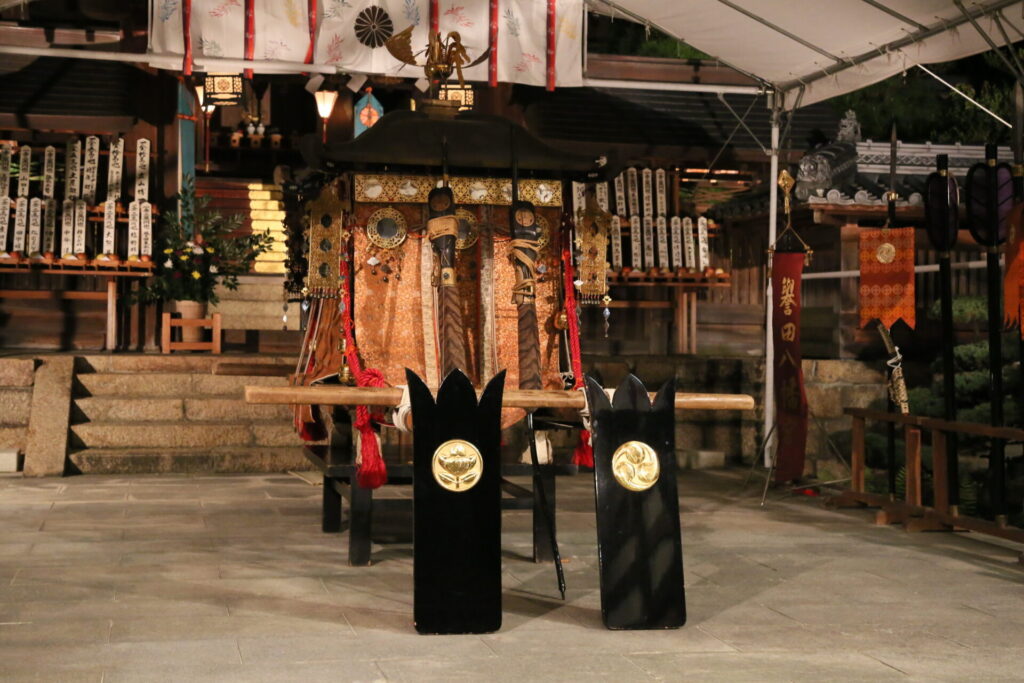 渡御の神事の前のお神輿です。飾り付けがなされ神輿の前には、三つ巴紋と橘の紋があしらわれた縦が設置されています。